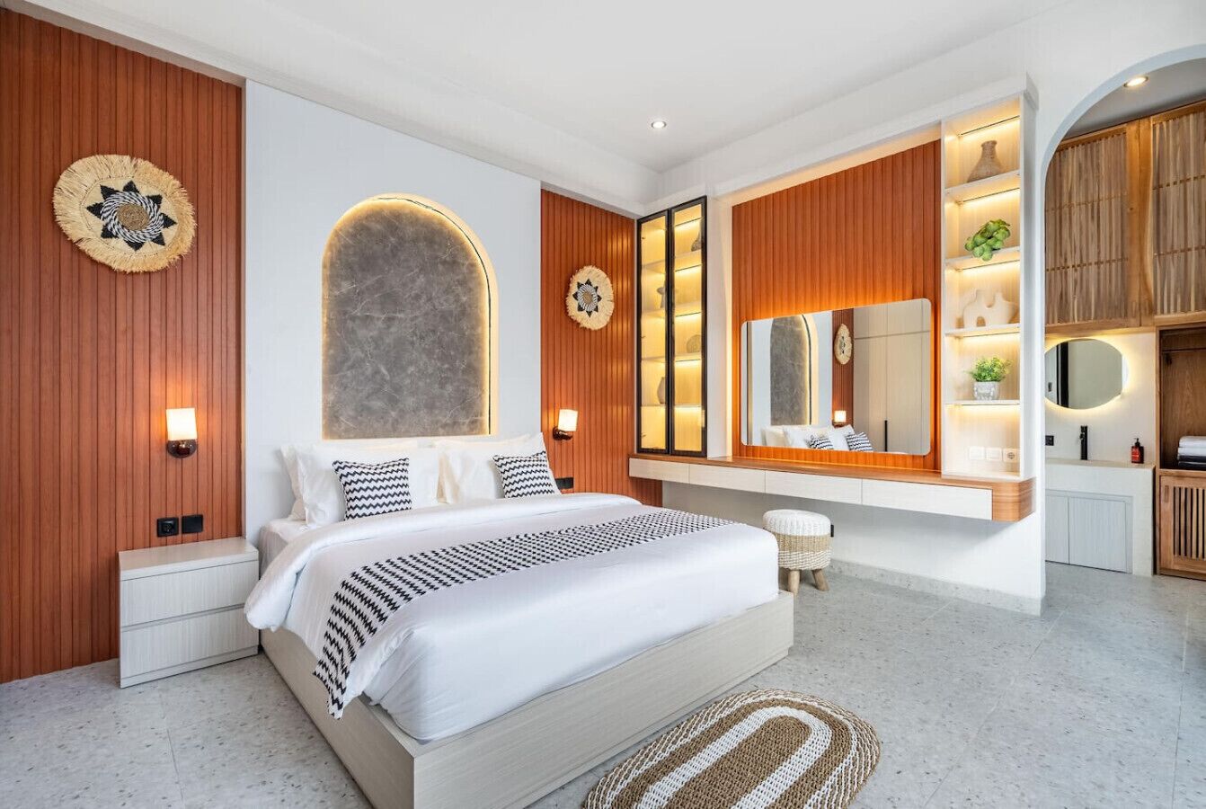 A modern bedroom with a large bed, wooden paneling, a built-in vanity, and a large mirror.