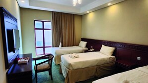 Une chambre d’hôtel avec deux lits simples, un bureau avec une chaise, une télévision et une fenêtre avec des rideaux.