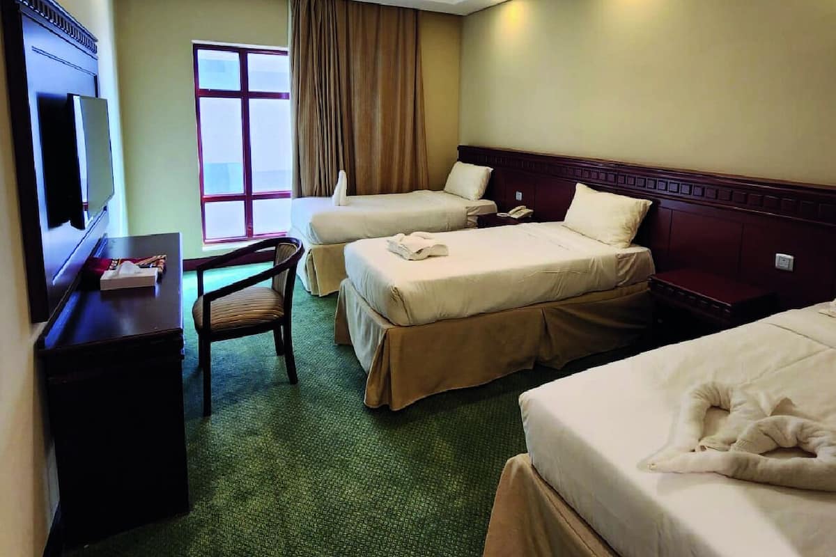 Une chambre d’hôtel avec deux lits simples, un bureau avec une chaise, une télévision et une fenêtre avec des rideaux.