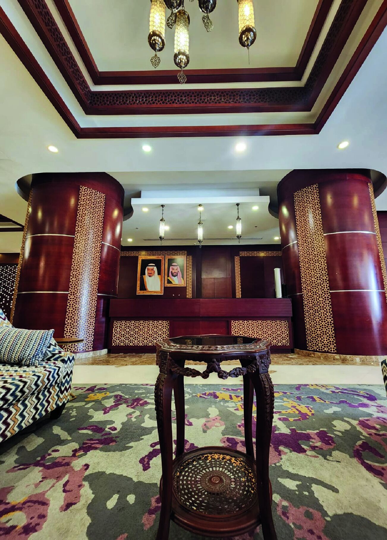 A lobby with a patterned carpet, a sofa, a table, and decorative columns.