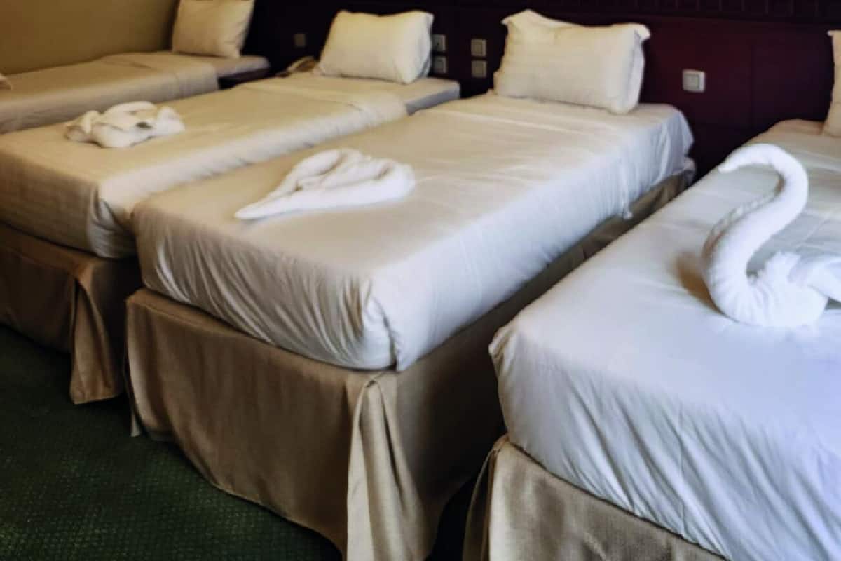 Une chambre d’hôtel avec trois lits, chacun étant équipé de draps et de serviettes blancs.