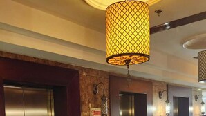 Un couloir doté d’ascenseurs, d’un sol en marbre et d’un luminaire décoratif suspendu au plafond.