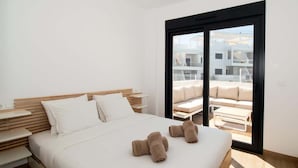 Une chambre d’hôtel moderne avec un grand lit, une tête de lit en bois et une vue sur un balcon aménagé avec du mobilier d’extérieur.