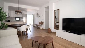 Un salon moderne avec un canapé, deux tables en bois, un téléviseur et une cuisine en arrière-plan.