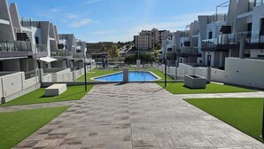 A modern building with a central pool, surrounded by a wooden deck and green lawns.