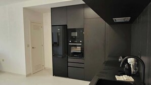A modern kitchen with a wooden accent wall, built-in appliances, and a black countertop.