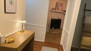 A hallway with a wooden bench, a small table with a lamp, a rug, and a framed picture on the wall.