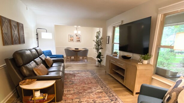 A living room with a leather sofa, a TV, a coffee table, and a dining area in the background.