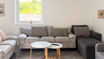 Ein Wohnzimmer mit einer Couch, zwei Beistelltischen, einem Fenster mit Jalousien und einer Zimmerpflanze.