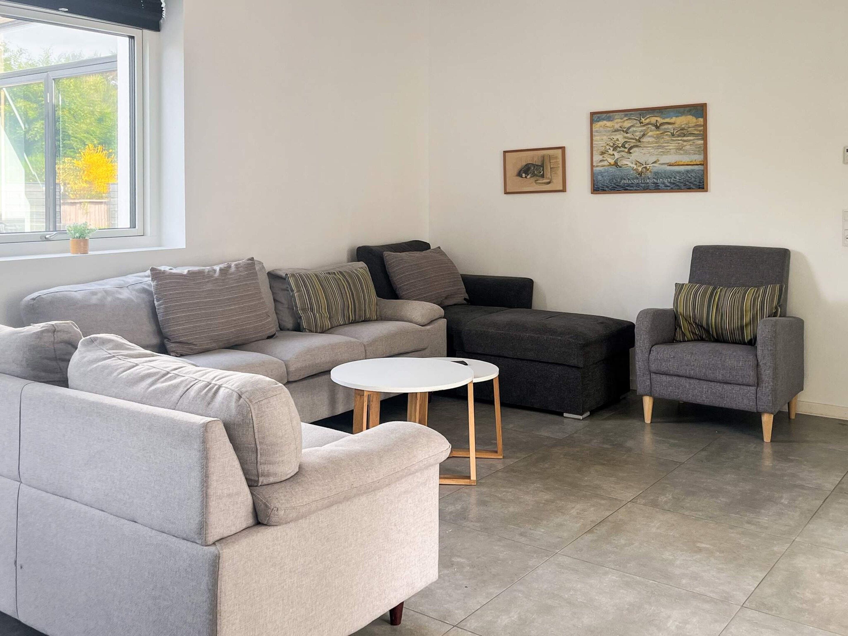 A modern living room with a grey sofa, a grey armchair, and a small white table.