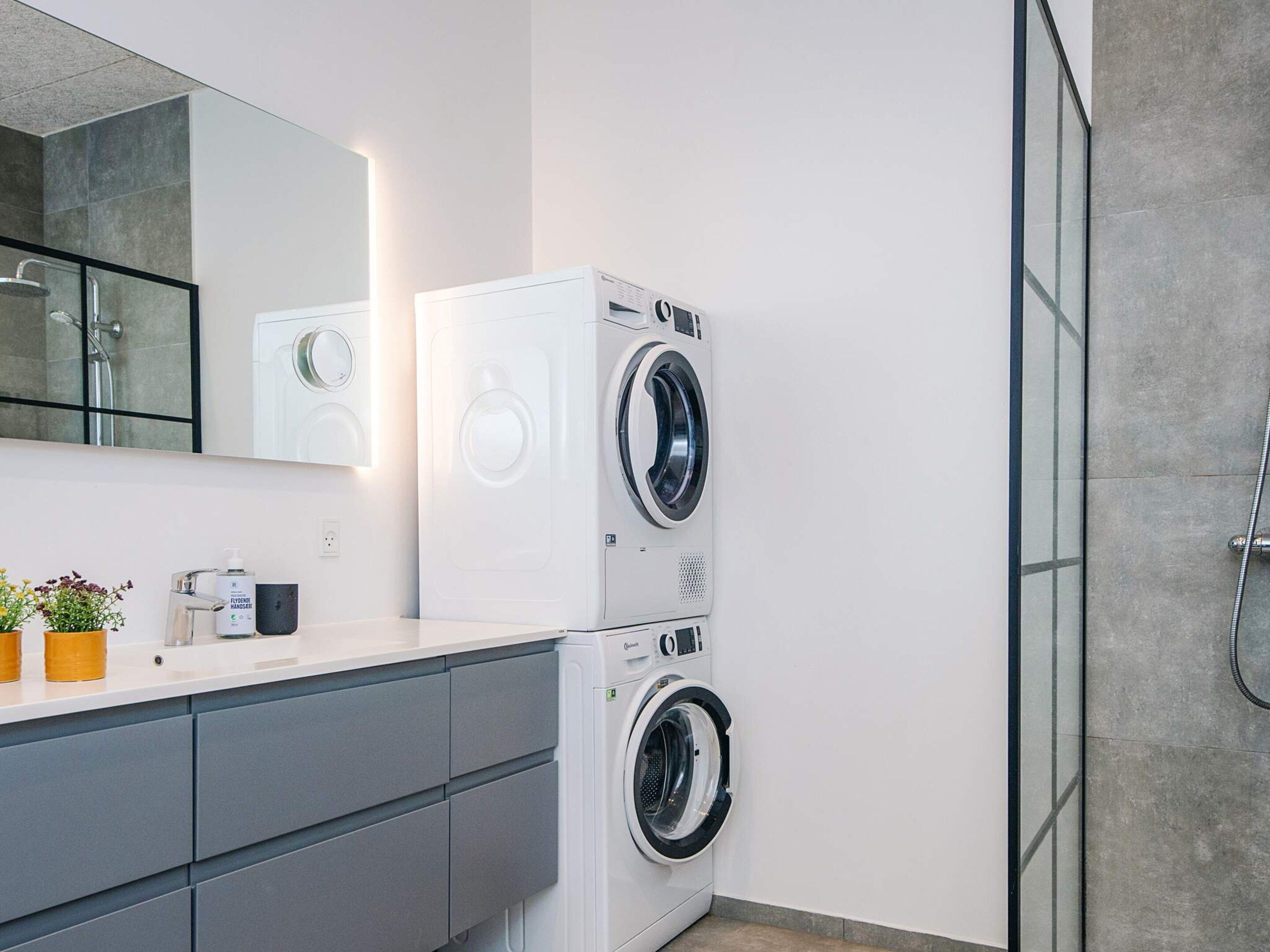 Une salle de bain moderne avec une douche à parois de verre, un lavabo blanc avec un miroir et un appareil combiné lave-linge et sèche-linge.