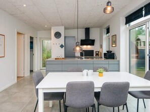 Une cuisine moderne dotée d’un îlot central, d’un coin repas avec une table blanche et des chaises grises, et d’une grande fenêtre offrant une vue sur l’extérieur.