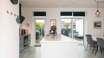 A modern kitchen with a central island, a dining area with chairs, and a large window providing a view of the outdoors.