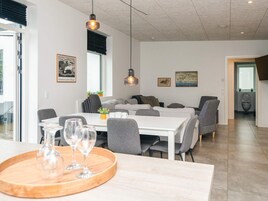 A modern dining area with a white table, grey chairs, and a wooden tray with glasses.