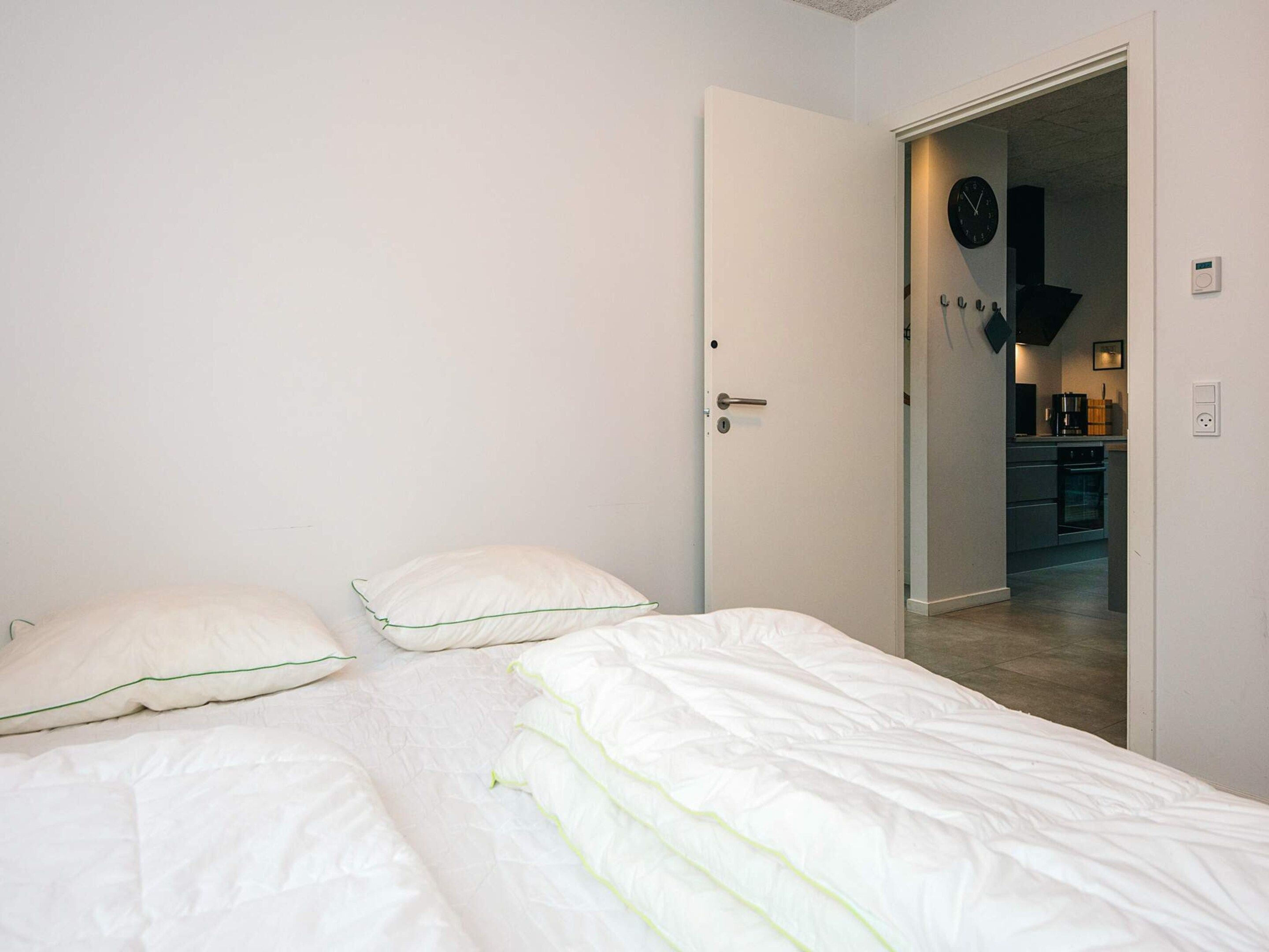 A bedroom with a bed, pillows, and a door leading to a kitchen area.