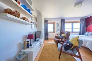 Une chambre d’hôtel moderne équipée d’un téléviseur à écran plat, d’un canapé, d’un lit, d’une petite table et d’une fenêtre avec des rideaux.
