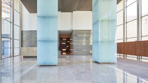 Eine geräumige Lobby mit Marmorboden, großen, hellen Säulen und Blick auf ein Gebäude.