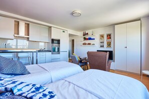 Une chambre d’hôtel moderne équipée d’une kitchenette, d’un lit avec une literie à motifs, d’un bureau avec une chaise et d’une armoire.
