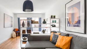 Ein modernes Wohnzimmer mit einem grauen Sofa, einer blauen Pendelleuchte und einem Bücherregal mit Dekorationselementen.