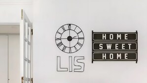 Ein Essbereich mit einem runden Tisch, durchsichtigen Stühlen, einer Wanduhr und einem Schild mit der Aufschrift 'HOME SWEET HOME'.