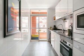 A modern kitchen with white cabinets, stainless steel appliances, and a large window.