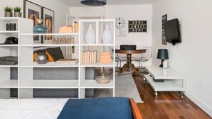 Ein modernes Schlafzimmer mit einem Bett, weißen Regalen, einem Schreibtisch und einem Esstisch.