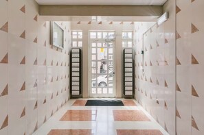 A hallway with patterned walls, a door with a window, and a black mat at the entrance.