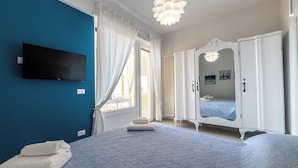 A bedroom with a bed, a TV mounted on the wall, a wardrobe, and a window with curtains. - Casinò Charme with Terrace by Wonderful Italy (Sanremo)