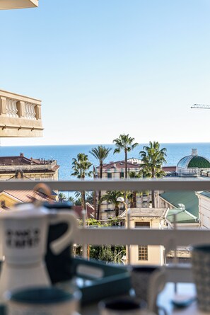 Een balkon met uitzicht op zee, palmbomen en gebouwen.