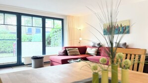 En moderne stue med et træbord, en rød sofa og et stort vindue med persienner.