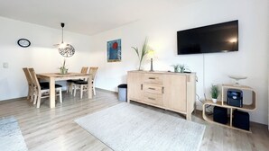 En moderne stue med spisebord, stole, et TV ophængt på væggen, et skab og en lampe.