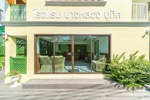 A building with a sign in a foreign language, large glass doors, and wicker furniture outside.