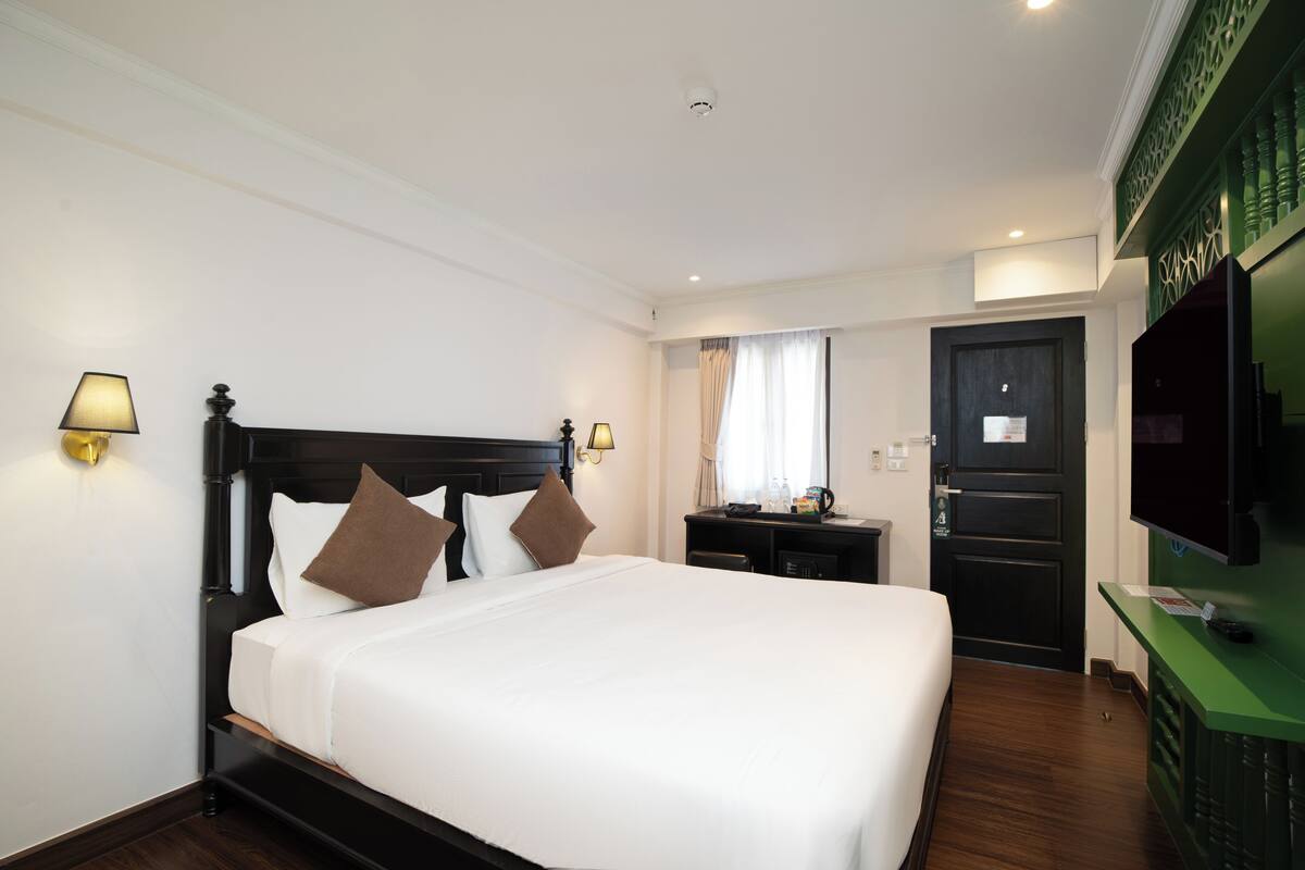 Une chambre d’hôtel avec un grand lit, des lampes de chevet, un bureau, une télévision et un mur d’accent de couleur verte.