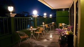 A patio area with outdoor seating and tables, a green fence, and decorative lighting. - Bangluang Boutique Hotel (Bangkok)