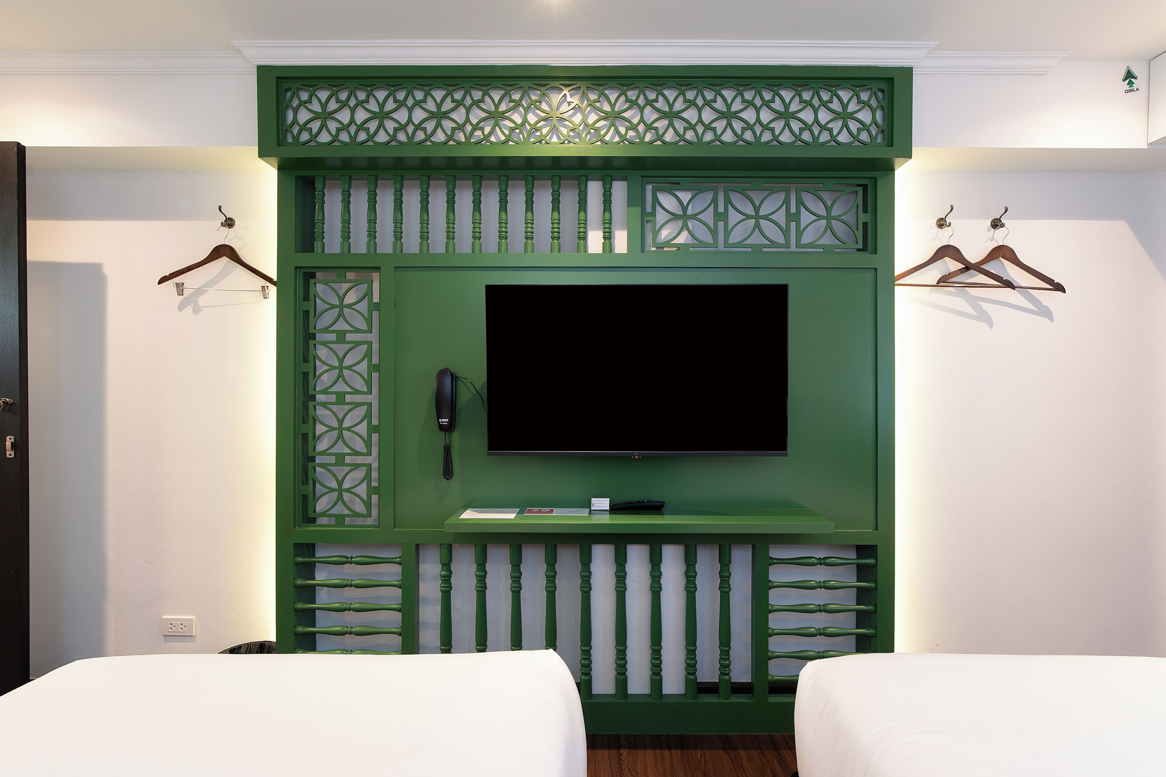 Una habitación con una pared verde decorativa, un televisor de pantalla plana, dos camas y un teléfono.