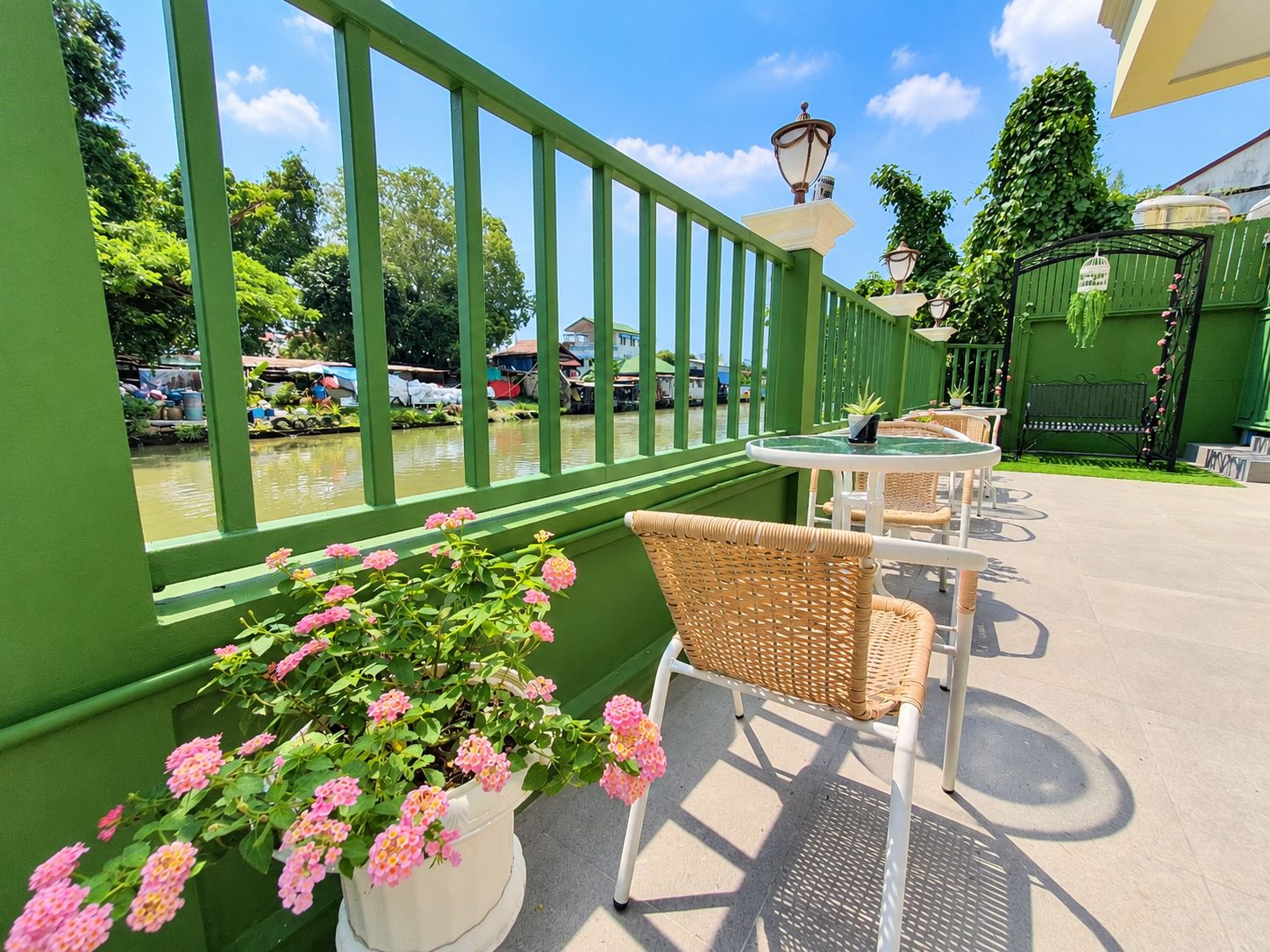 A green outdoor seating area with wicker chairs and a table, overlooking a body of water with boats.