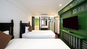Une chambre d’hôtel avec deux lits, un téléviseur fixé sur un mur vert, une salle de bain visible à travers une porte ouverte et une caméra de surveillance fixée au plafond.