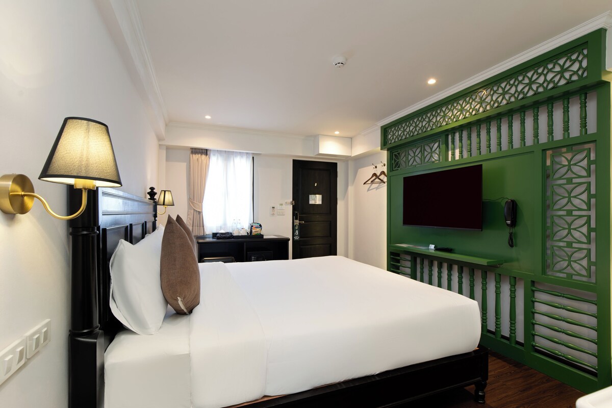 Una habitación de hotel con una cama, un escritorio, una lámpara, un televisor y una pared decorativa verde.