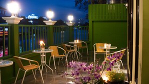 Une terrasse avec des sièges extérieurs, comprenant des chaises et des tables en osier, et offrant une vue sur le paysage urbain la nuit.