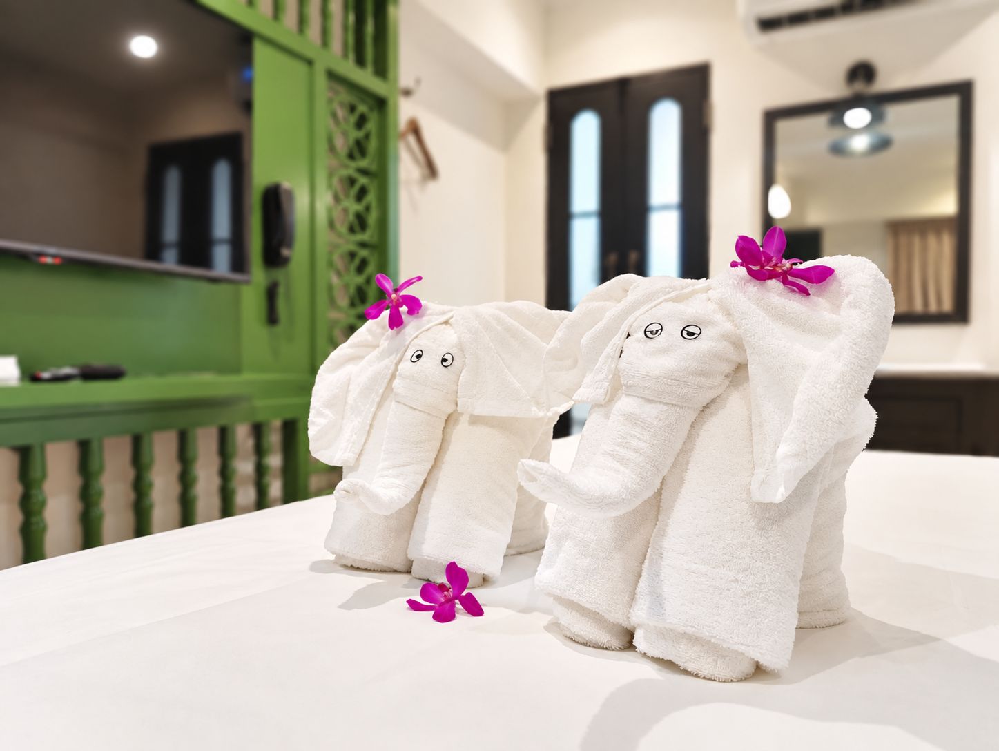 Two plush elephant-shaped towels with bows on a white surface, likely in a hotel room.