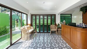 Un hall d'hôtel avec un comptoir d'accueil, deux fauteuils en osier, un ordinateur portable et un sol à motifs.