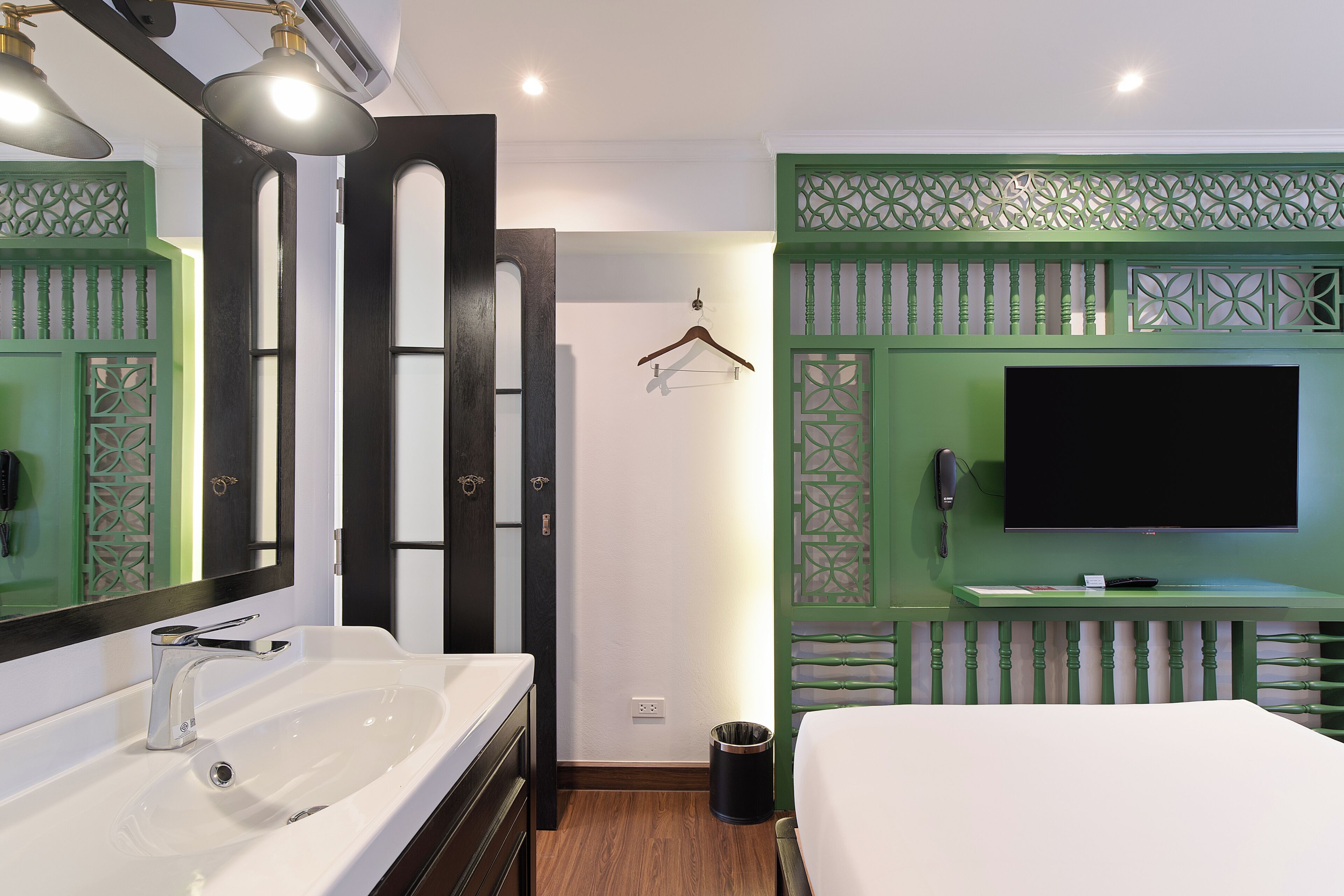 A hotel room with a white sink, a bed, a TV, and a green decorative panel.