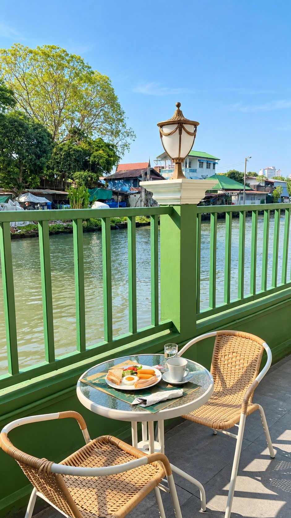 A balcony with a table and chairs overlooking a water body, with a lamp post and buildings in the background.