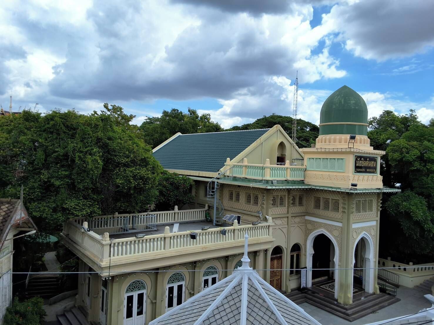 A mosque with a green dome and a beige facade, surrounded by lush greenery.