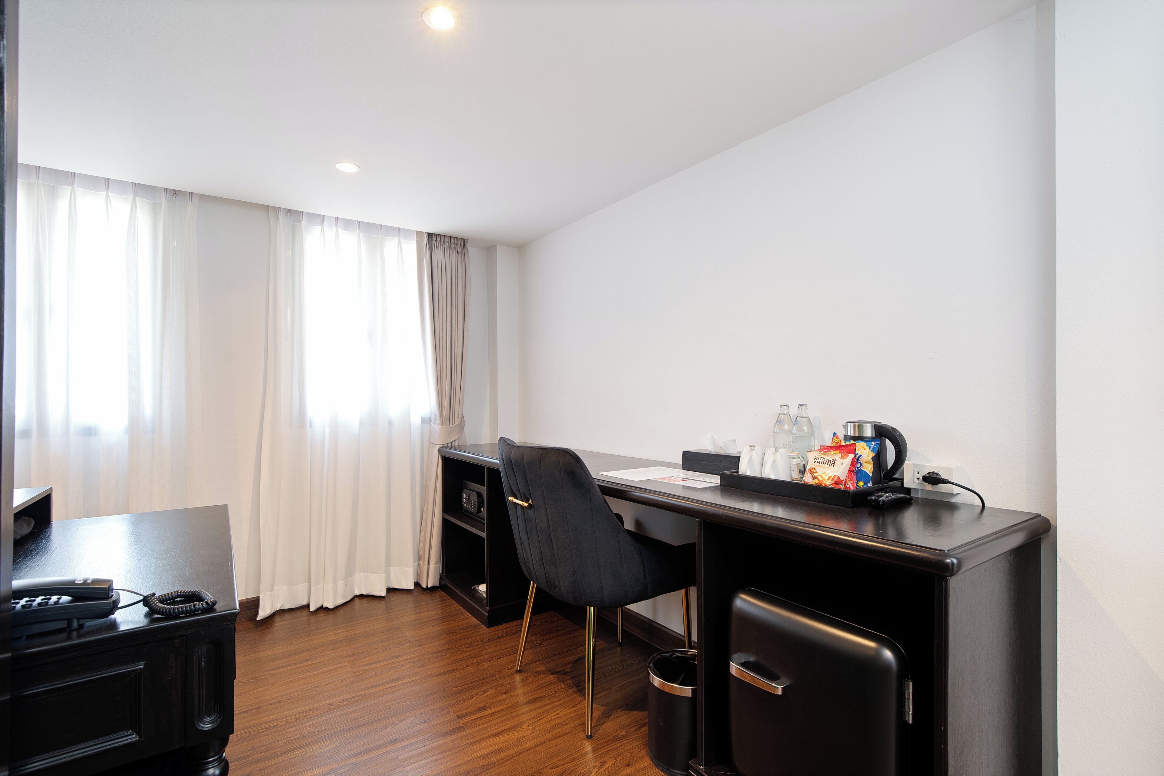 A hotel room with a desk, chair, and a small refrigerator.