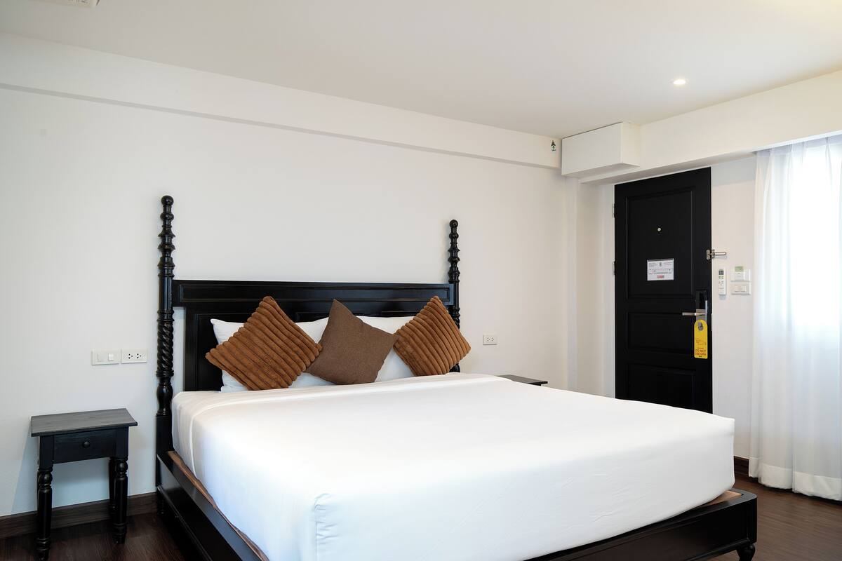 Une chambre d’hôtel avec un grand lit, une table de chevet, une porte noire et un rideau blanc.