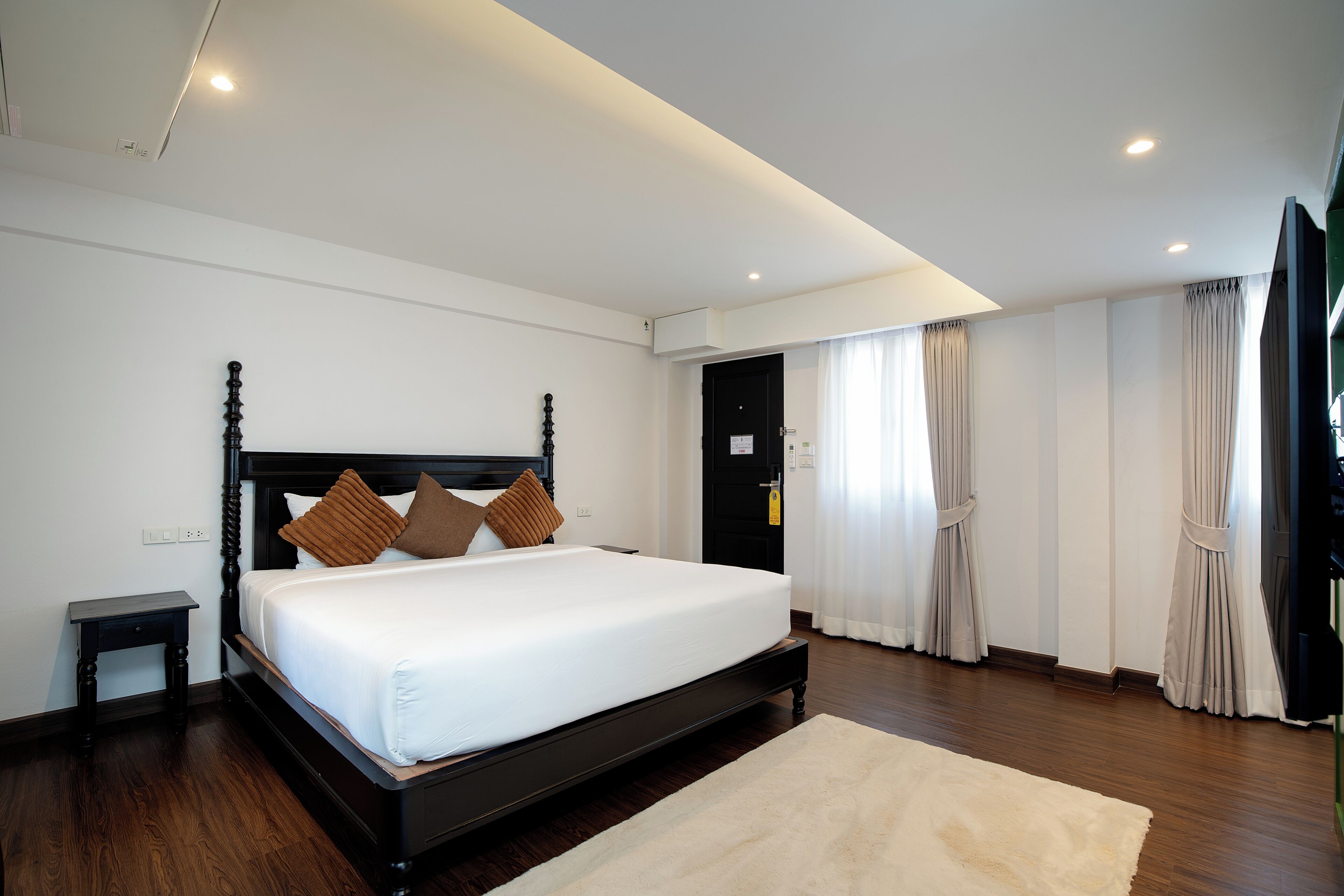 A bedroom with a large bed, a nightstand, a flat-screen TV, and a door leading to another room.