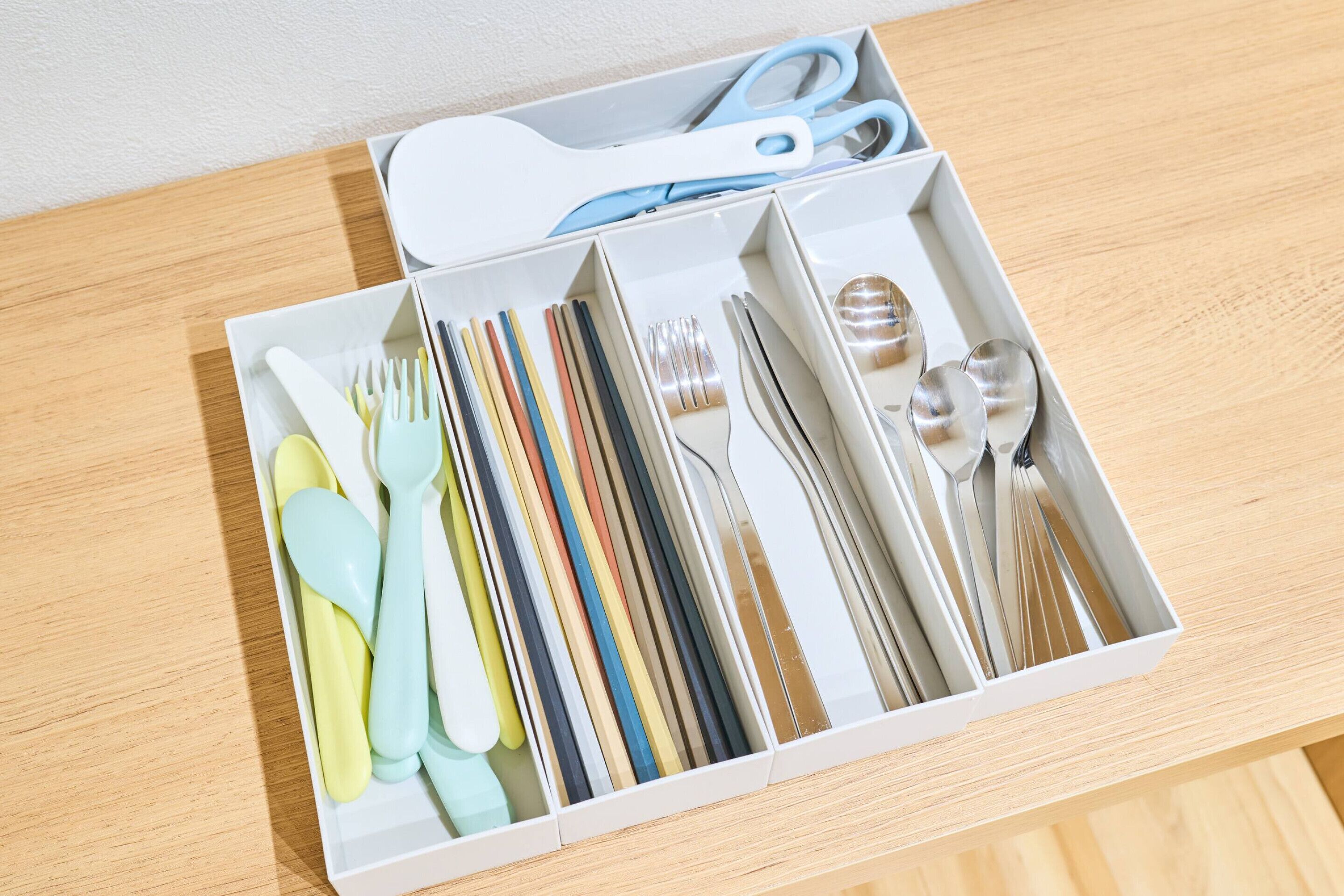 Uma gaveta com utensílios organizados, incluindo colheres, garfos e facas, além de um par de tesouras.