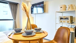 A hotel room with a dining table set with blue and white patterned bowls, a vase with dried plants, and a television mounted on the wall.