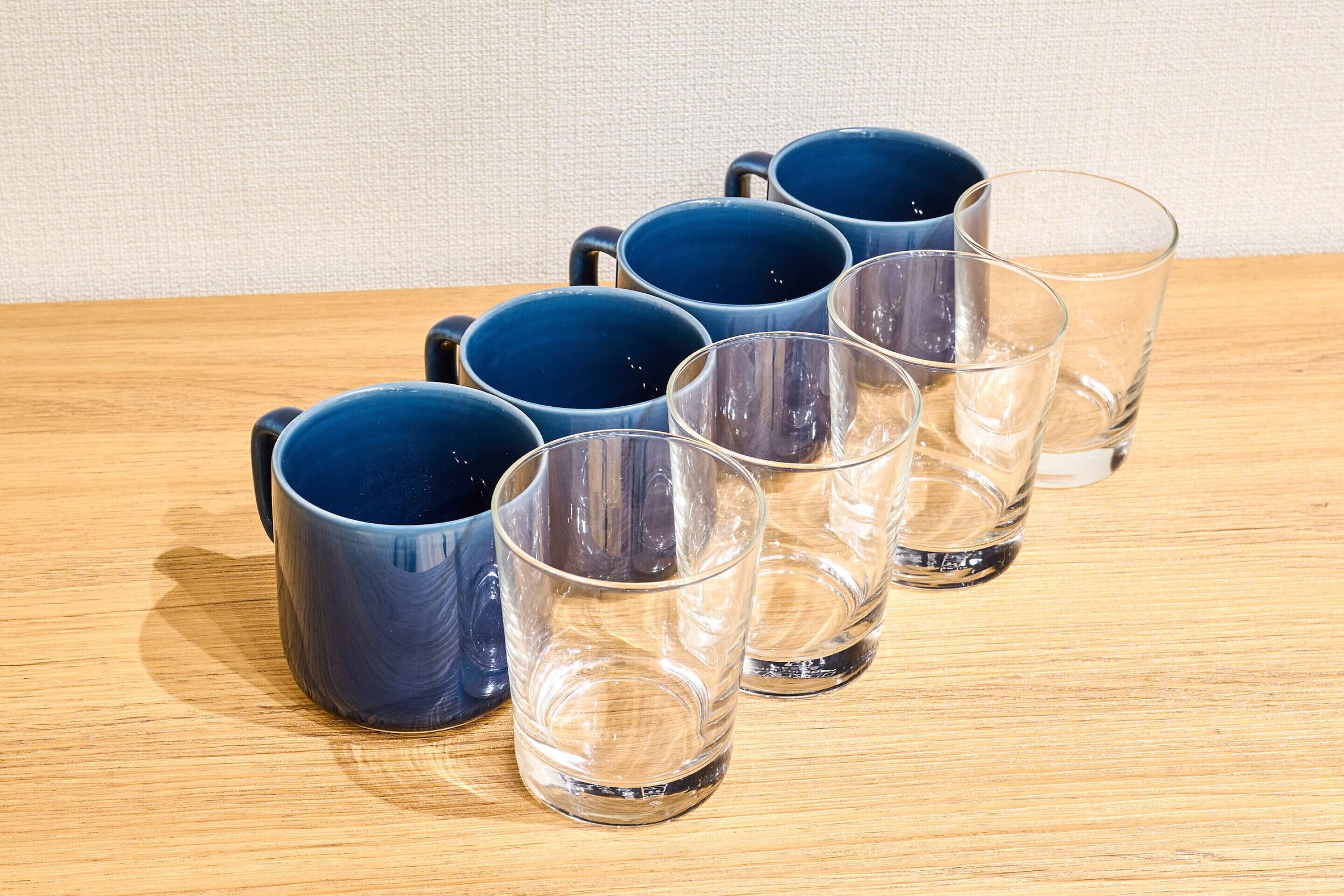 A set of six blue mugs and four clear glasses arranged on a wooden surface.